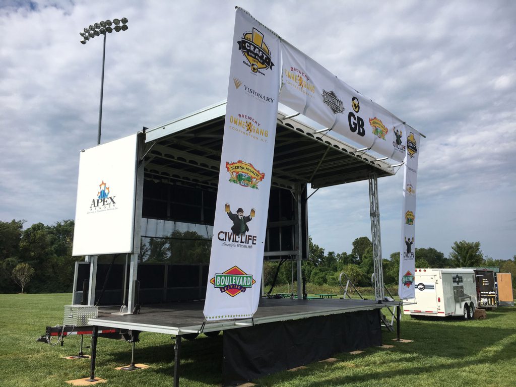 Apex stage on grassy field with Craft Beer festival and Apex Stages logo on white wing panel, sponsor banners