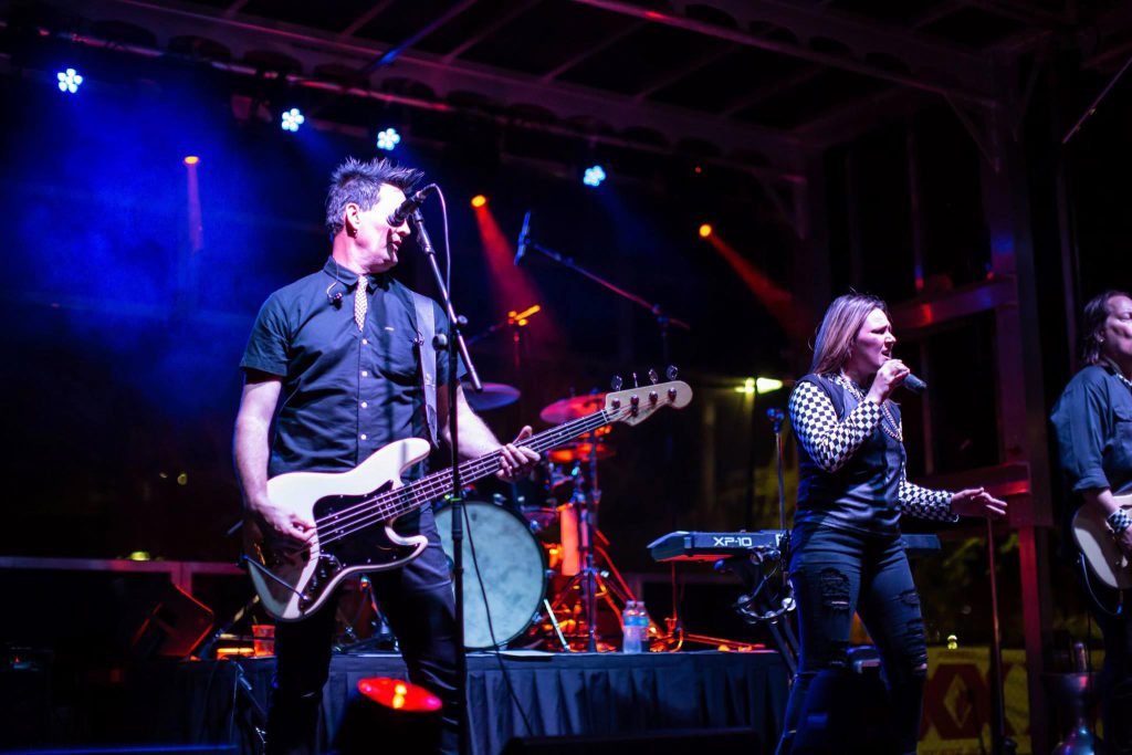 Guitarist and female vocalist performing under colorful stage lighting on Apex stage