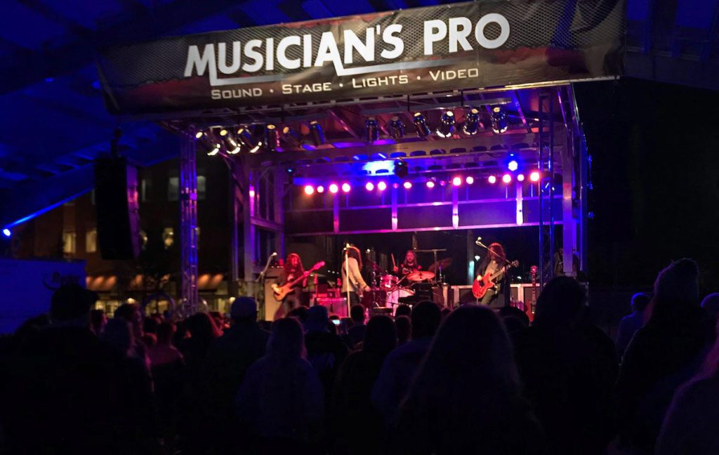 Musician's Pro branded Apex stage with rock band performing at night, crowd in foreground
