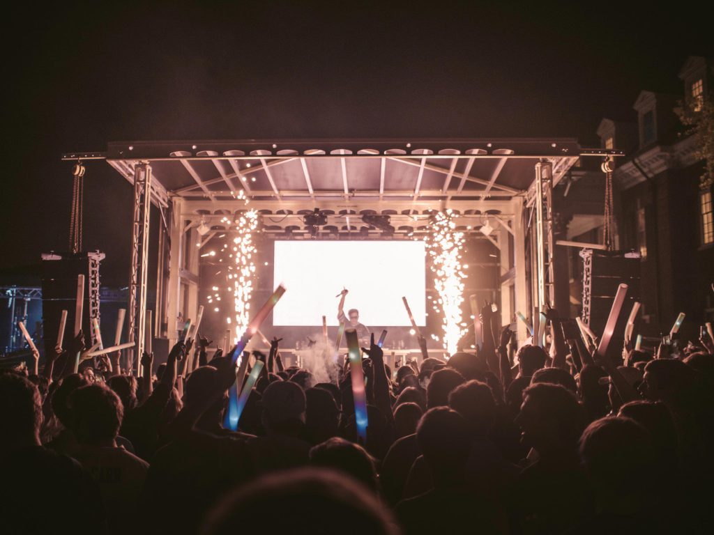 Night show with pyrotechnics and crowd raising glow sticks, performer on Apex stage