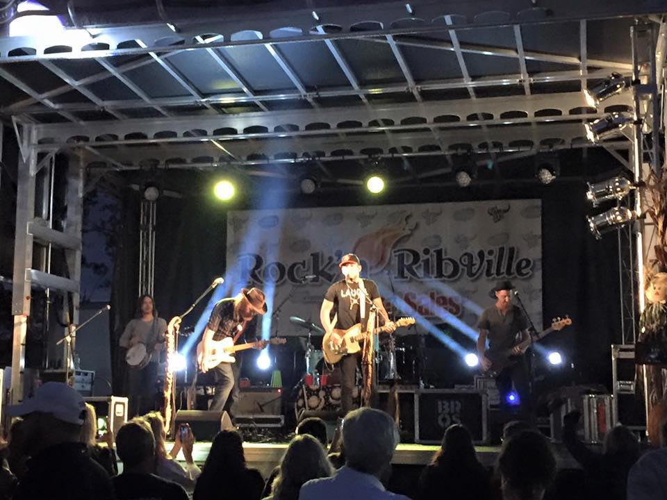 Rock band performing at night at Rock'n Ribville with dramatic light beams on Apex stage