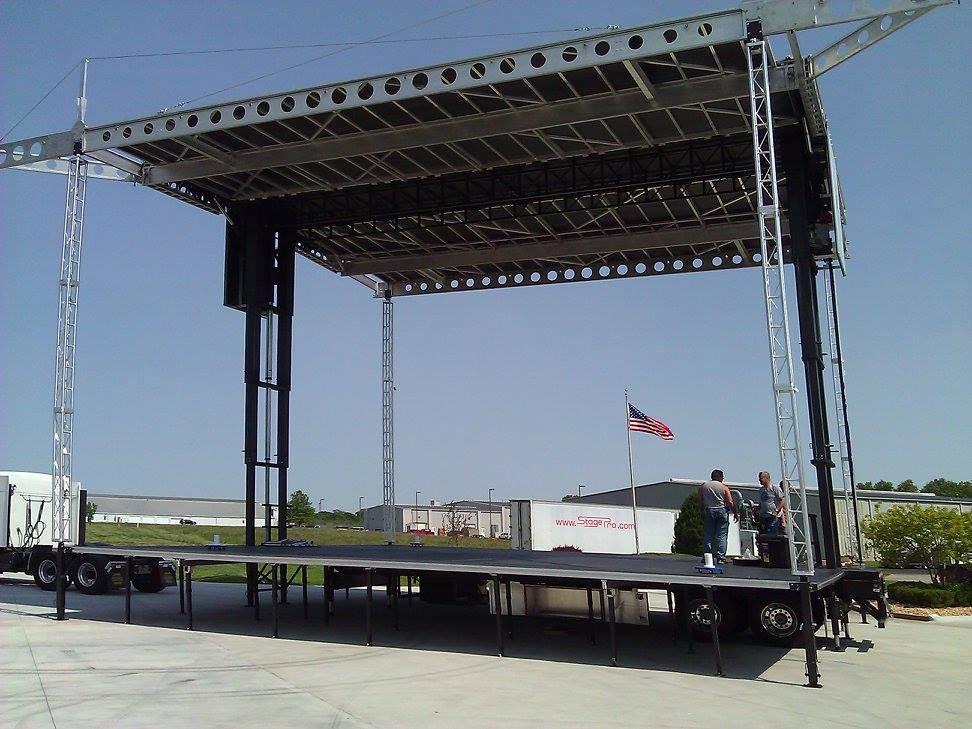 Apex 42x20 stage deployed at industrial lot with American flag and two crew members