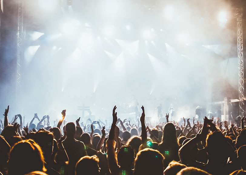 Festival crowd with raised hands in front of a brightly lit concert stage