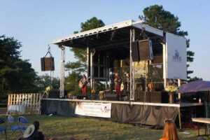 APEX 2016 mobile stage at an outdoor benefit concert, with a duo performing and Apex Stages branding on the side panel