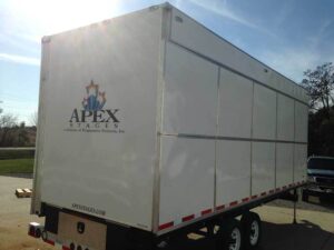 Apex Stages mobile stage folded into its trailer and parked outside, with the Apex Stages logo on the rear door