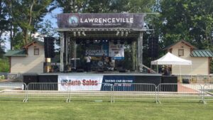 APEX 2420 mobile stage on a lawn with a Lawrenceville summer concert series banner across the roof header