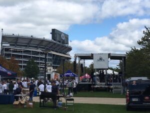 APEX 2420 mobile stage set up for a tailgate event on the lawn outside a college football stadium