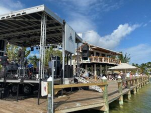 APEX 2420 mobile stage positioned on a waterfront dock beside a covered bar, with the deck facing the walkway