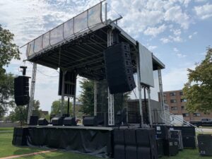 Three-quarter view of the APEX 2424 mobile stage showing the flown line array and the trailer body behind the deck