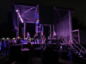 Band performing on the APEX 2424 mobile stage at night, lit in purple with an LED screen behind them