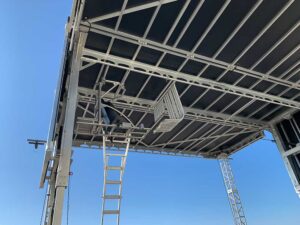 Underside of the APEX 2424 mobile stage roof canopy, showing the aluminium truss framing and an access ladder