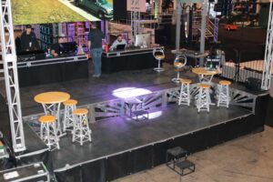 APEX 2424 mobile stage set up indoors as a lounge, with high tables and stools arranged on the deck