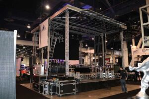 APEX 2424 mobile stage on display at an indoor trade show, with road cases stacked beside the deck