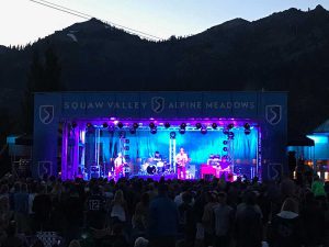 APEX 3224 GEN5 mobile stage lit in purple for an evening concert below a mountain ridge, with a standing crowd