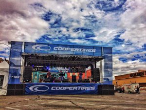 APEX 3224 GEN5 mobile stage dressed in Cooper Tires branding for a street event under a cloudy sky